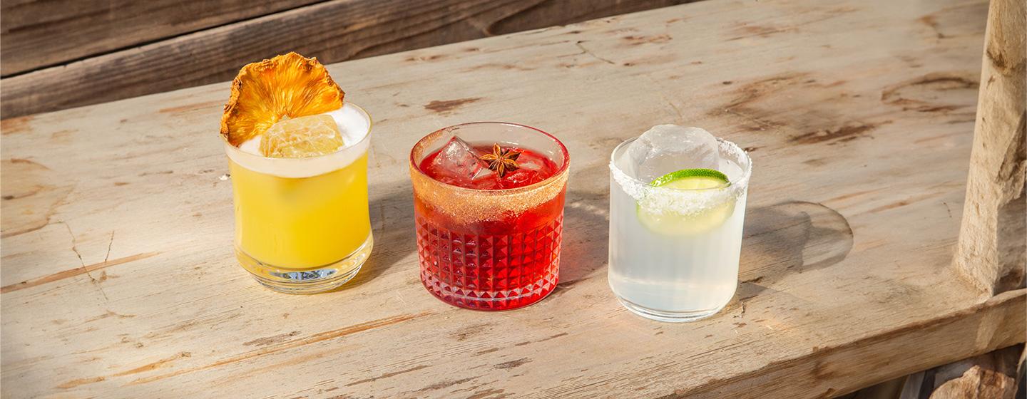 Three cocktails on a wood plank