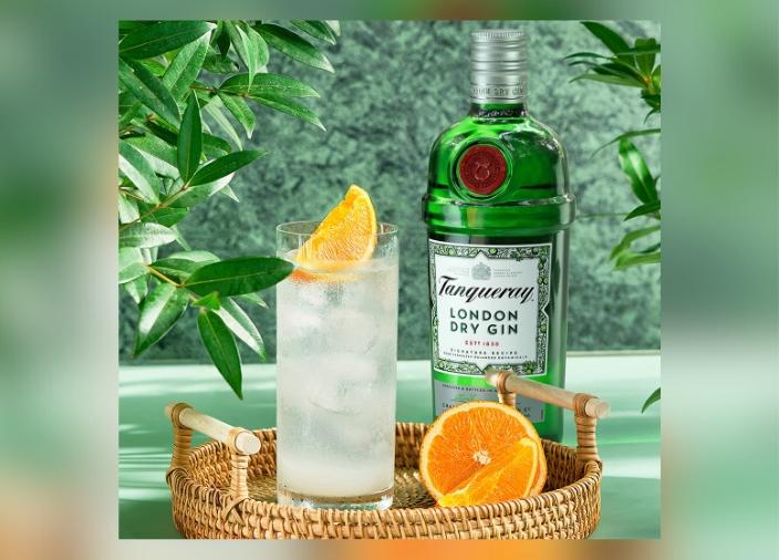 Garrafa de Tanqueray London Dry Gin ao lado de um coquetel em um copo highball em uma bandeja com uma laranja