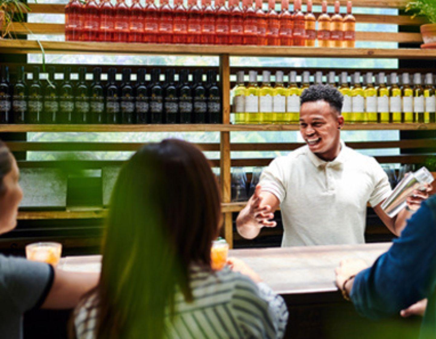 Bartender with a cocktail shaker interscting with customers sitting at the bar.