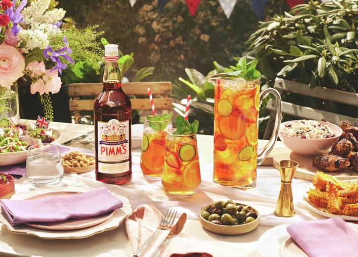 Eine Flasche Pimm's steht auf dem Tisch, daneben zwei Gläser mit Cocktails und ein Teller mit Chips. 