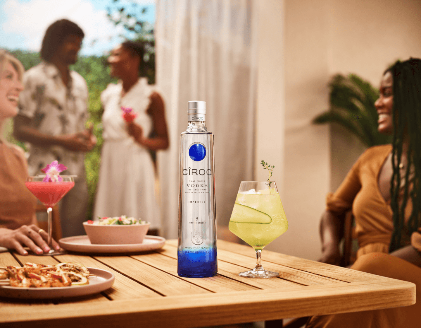Bottle of CÎROC on table beside cocktail glass and assorted plates of food 