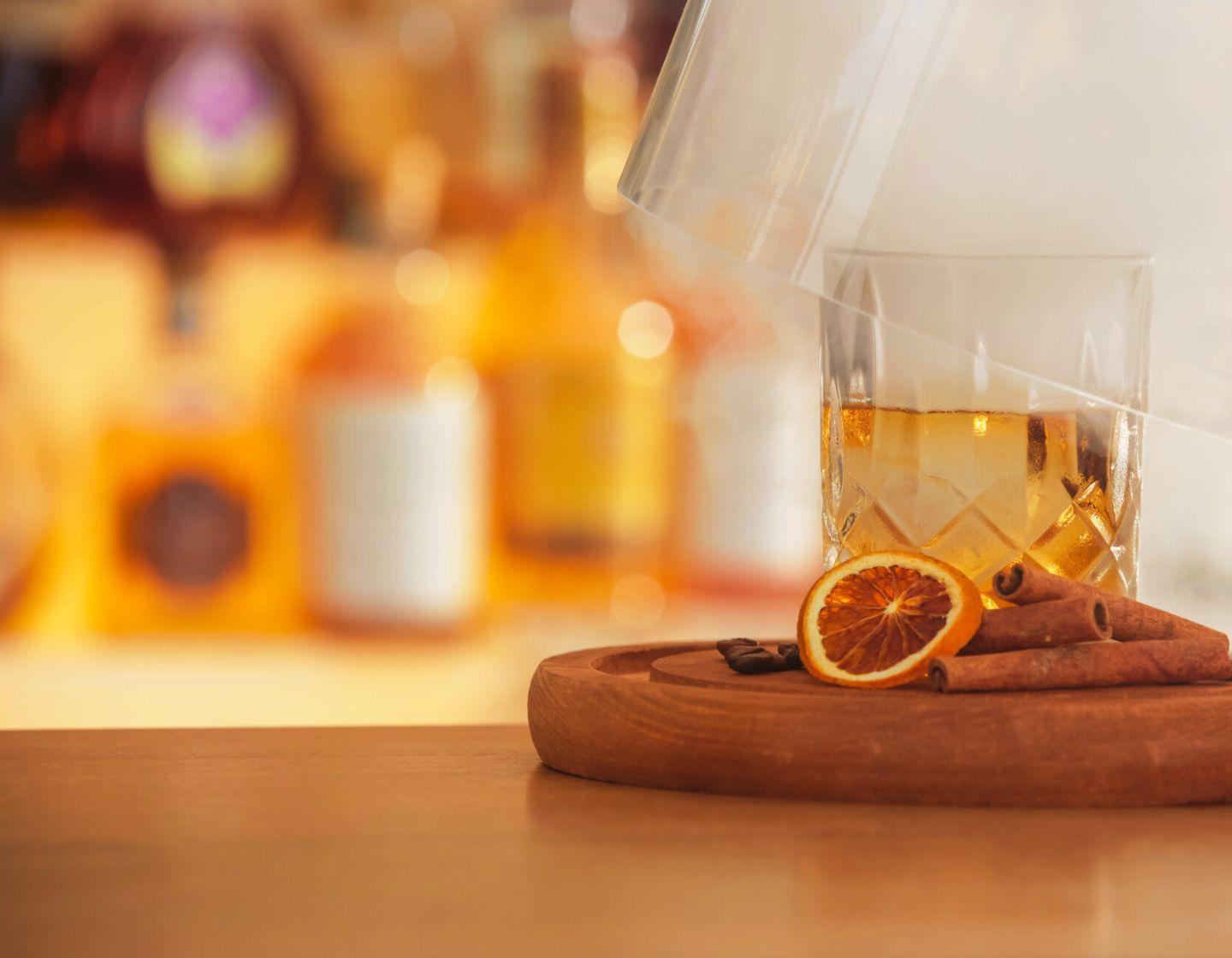 A clear tumbler glass filled with liquid with a dried orange garnish.