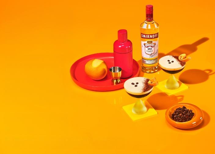 Eine Flasche Smirnoff No.21 mit zwei Espresso Martinis und Zutaten auf einem orangefarbenen Hintergrund