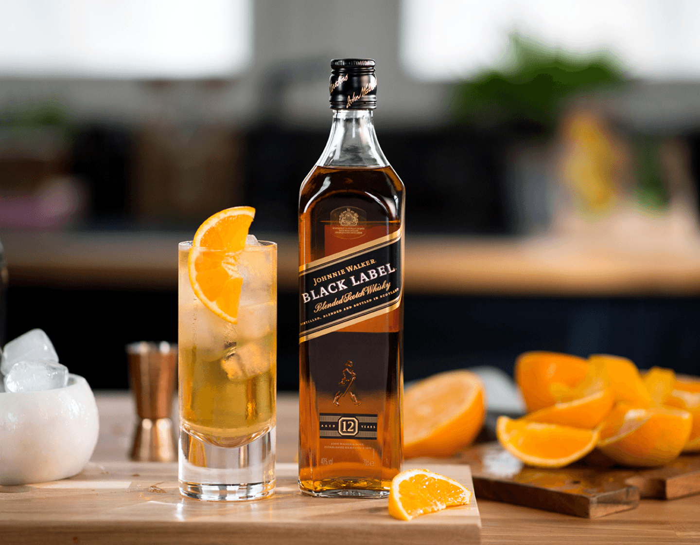 Bottle of Johnnie Walker Black Label whisky on chopping board beside cocktail surrounded by sliced oranges. 