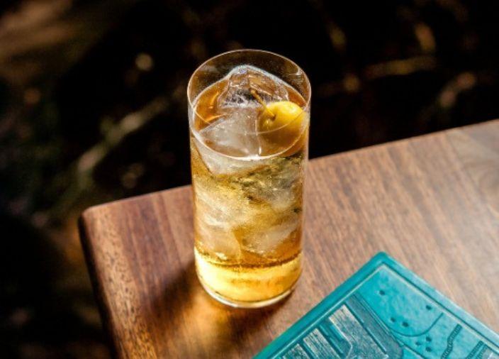 A highball cocktail with ice cubes and an olive garnish.
