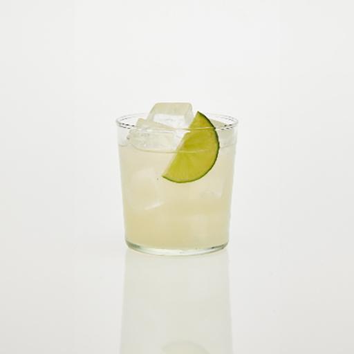 Ein Gin Rickey in einem Eis gefüllten Highball-Glas mit einer Limettenspalte, arrangiert auf einem Holztisch. Umgeben von Zutaten: Eiswürfel, Limettenspalten, Eis und Kräutern.