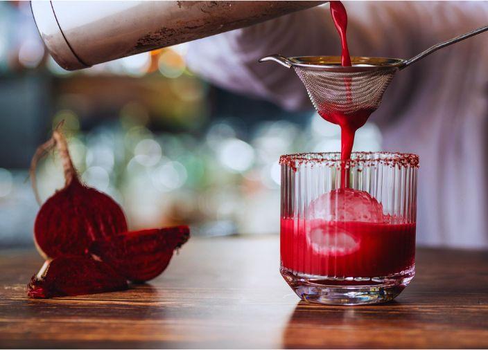 Red cocktail being strained into a glass with ice.