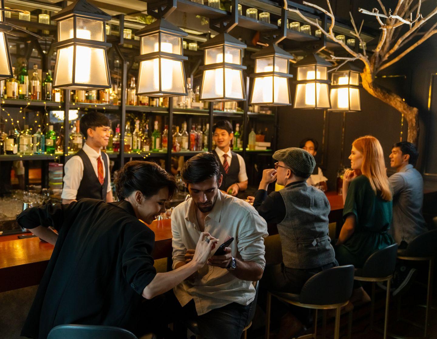Bar movimentado com dois bartenders servindo os convidados 