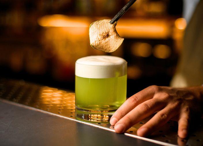 Green foam cocktail being garnished with dried fruit.