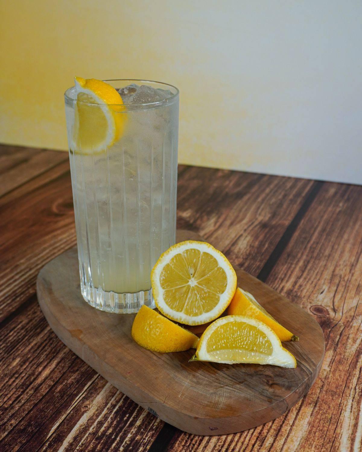 Una botella de ginebra Gordon’s Sicilian Lemon junto a dos copas de gin-tonic sobre un fondo azul 