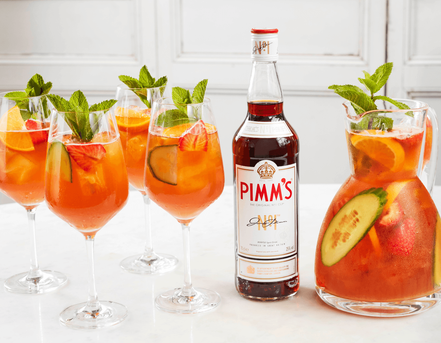 Bottle of Pimm’s next to four cocktail glasses and a pitcher.