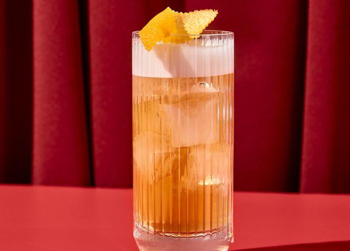 Cóctel de whisky de naranja en vaso alto adornado con fruta.