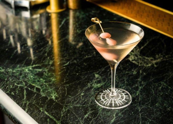 A martini drink with a pink pickle garnish.