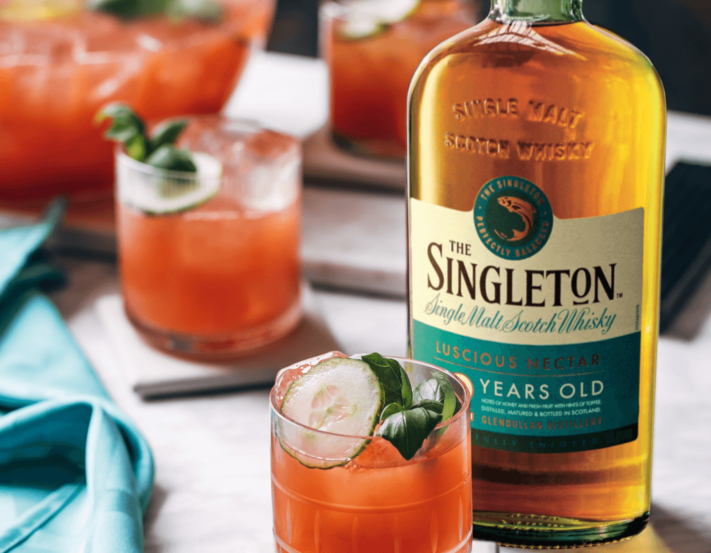 Bottle of The Singleton whiskey on table beside red cocktail 