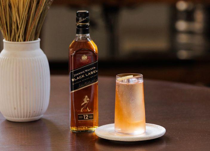 Cóctel de color naranja con hielo acompañado de una botella de licor.