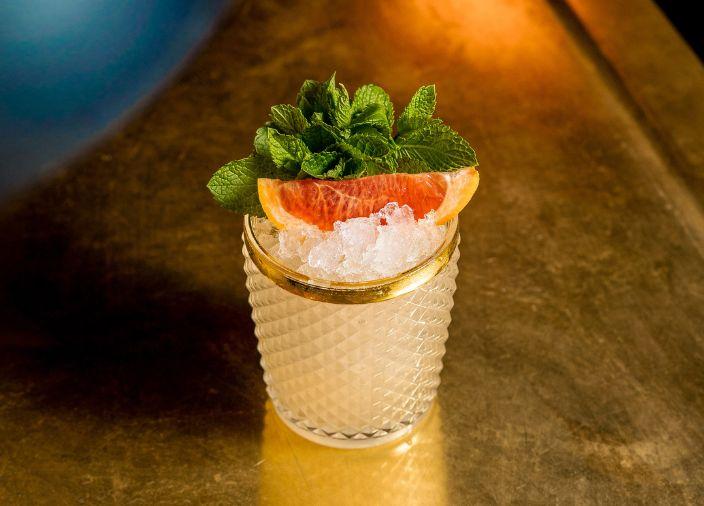 Un cóctel de naranja con ramitas de menta y una rodaja de pomelo para decorar.