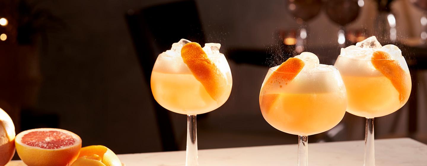Three cocktails with orange garnish and foam