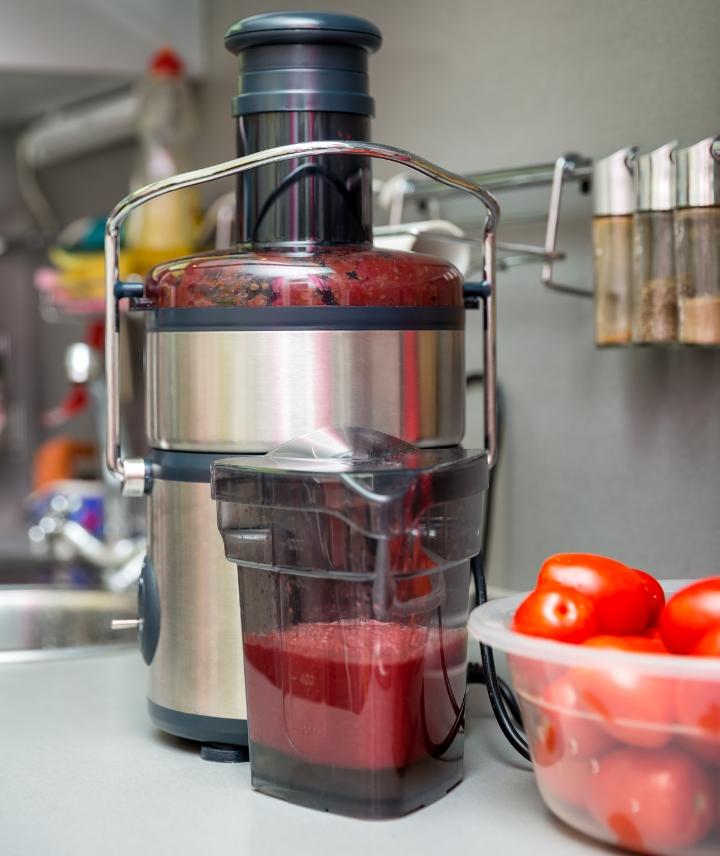 Juicer making tomato juice in kitchen with basket of fresh tomatoes