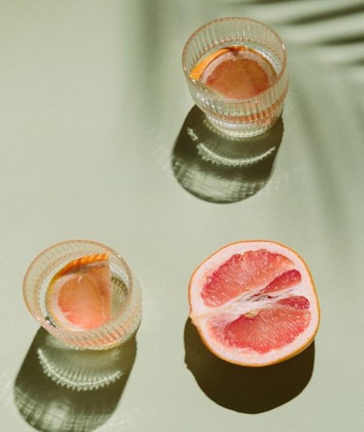 Zwei Getränke sind mit einer pinken Grapefruit auf einem grünen Untergrund
