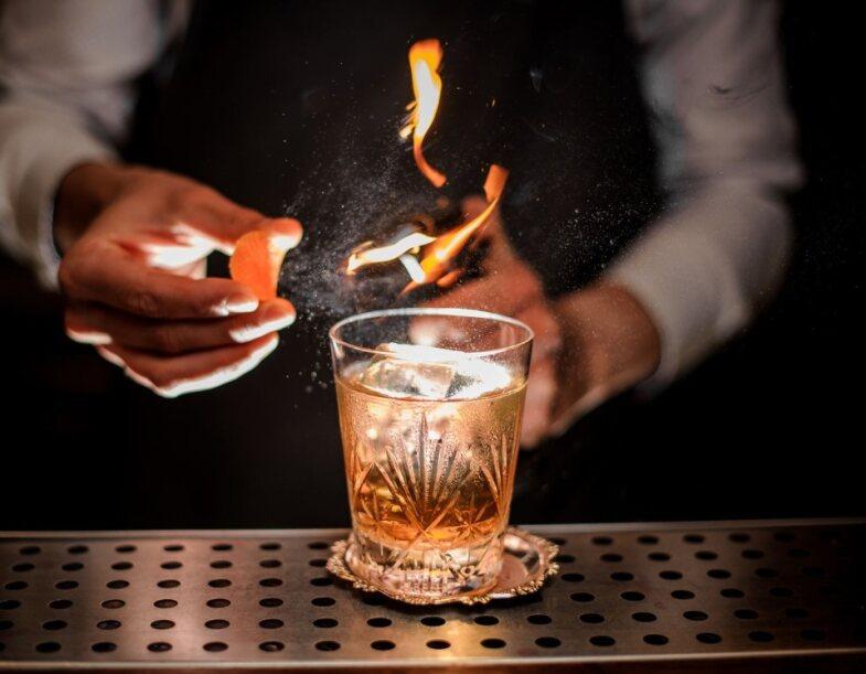 A bar staff member making a whisky cocktail using fire.