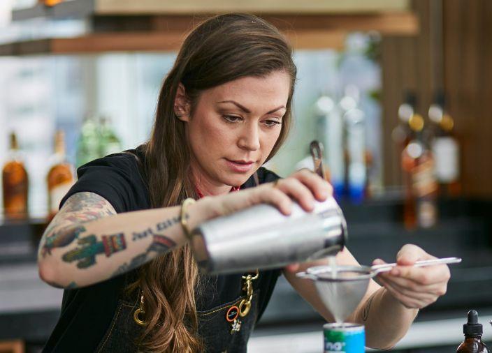 Mujer sirviendo una bebida utilizando herramientas de bar.