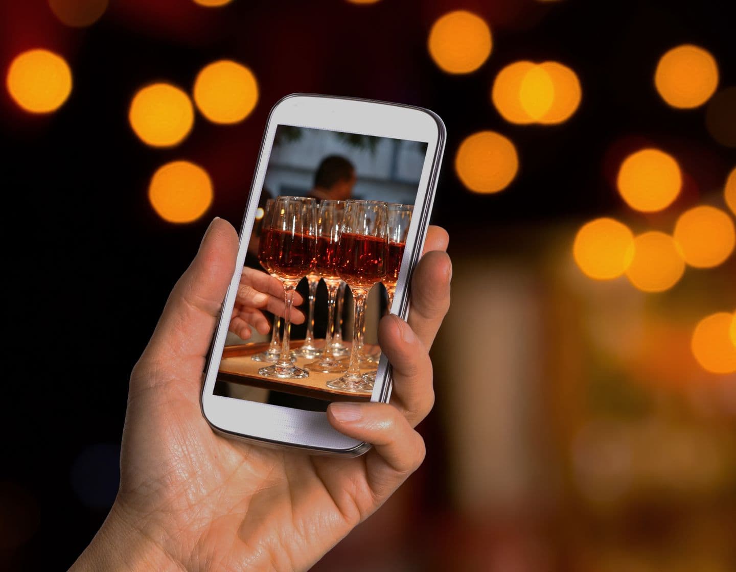 Mano sosteniendo el teléfono con foto de copas de vino.