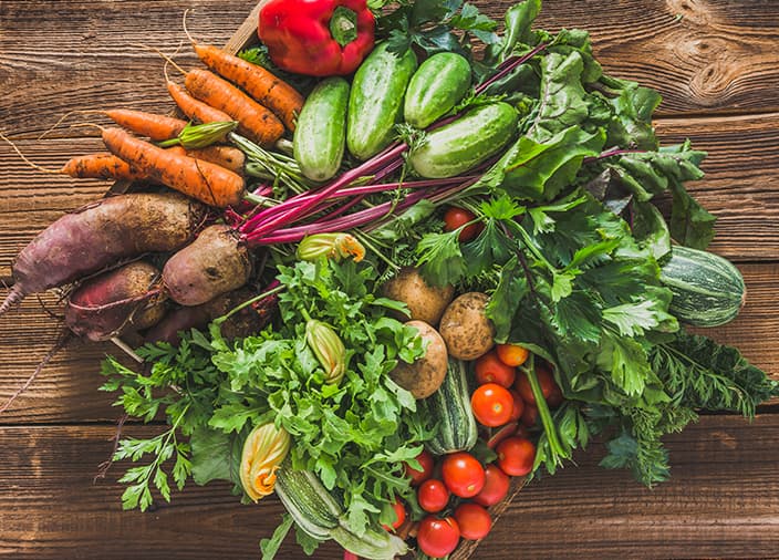 Una colección de verduras, zanahorias, remolachas, pepinos, tomates, calabazas y más, reunidas en círculo encima de una mesa de madera.