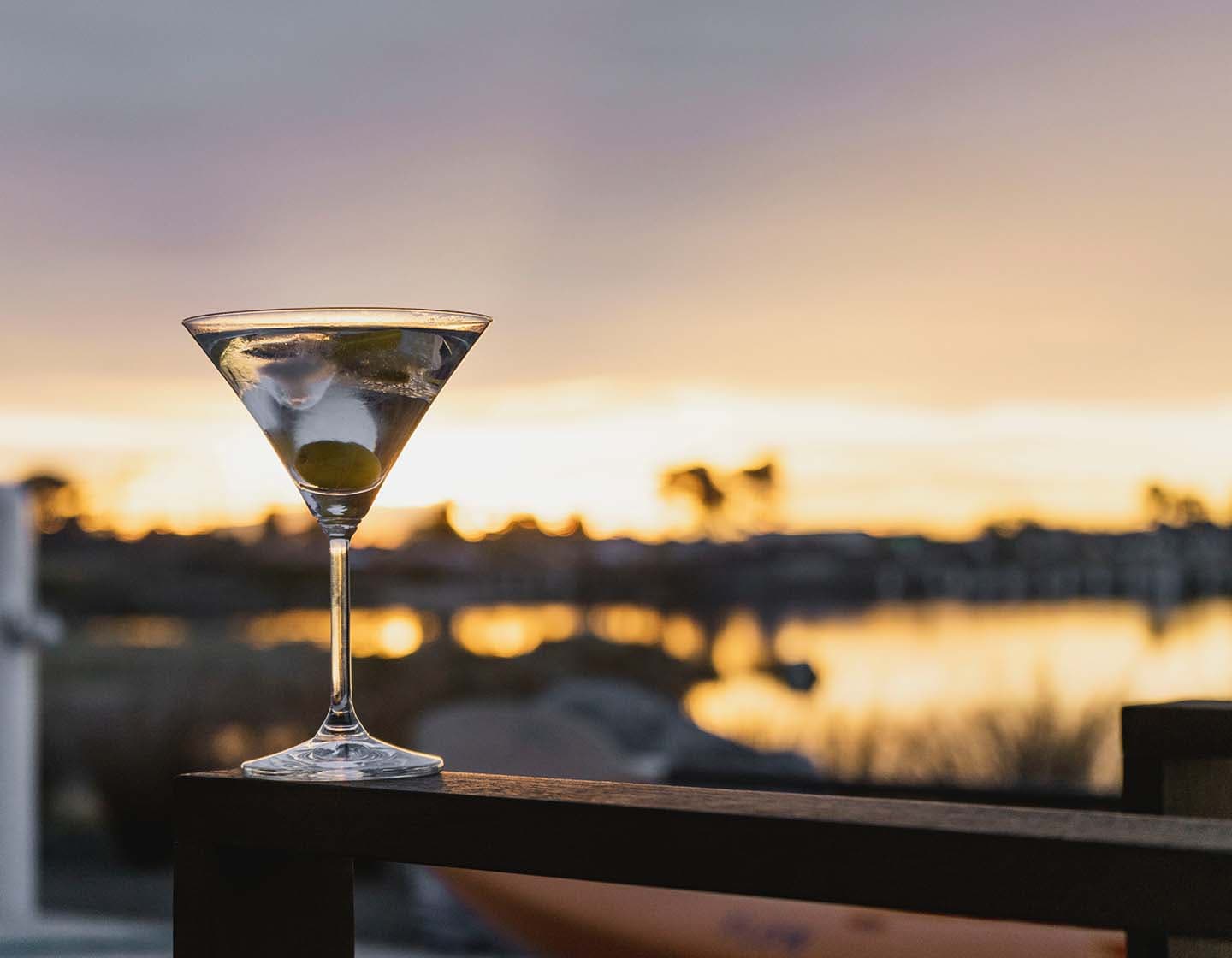 A Dirty Martini, with olives in the glass against a sunset background. 