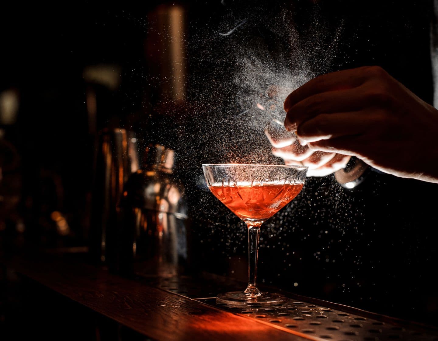 Bartender garnishing an orange cocktail in dim lighting 