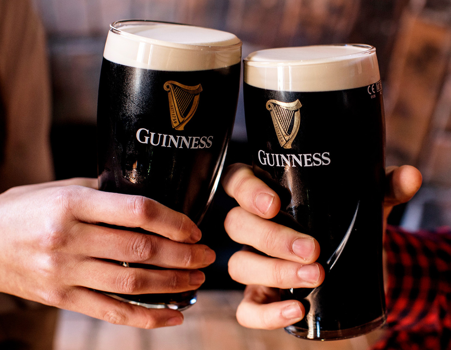Dos manos brindando con dos vasos de pinta de Guinness.