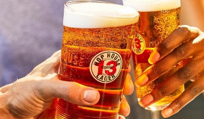 Two hands ‘cheersing’ pint glasses of Hop House 13 Lager
