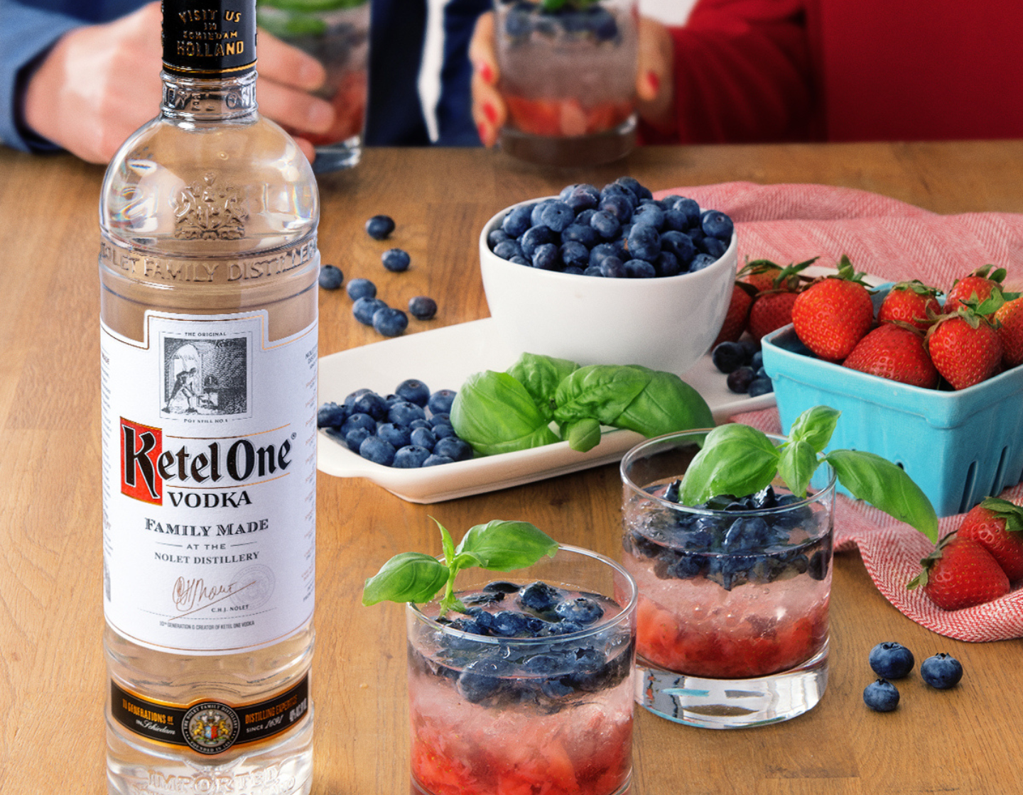 Bottle of Ketel One Vodka on a table surrounded with fresh fruits strawberries and blackberries 
