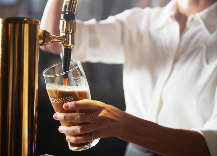 Un bartender sirviendo una pinta de Guinness en un vaso de Guinness.