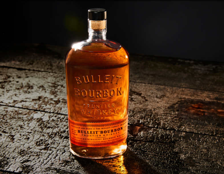 Botella de Bulleit Bourbon con un vaso adornado sobre una superficie de madera.