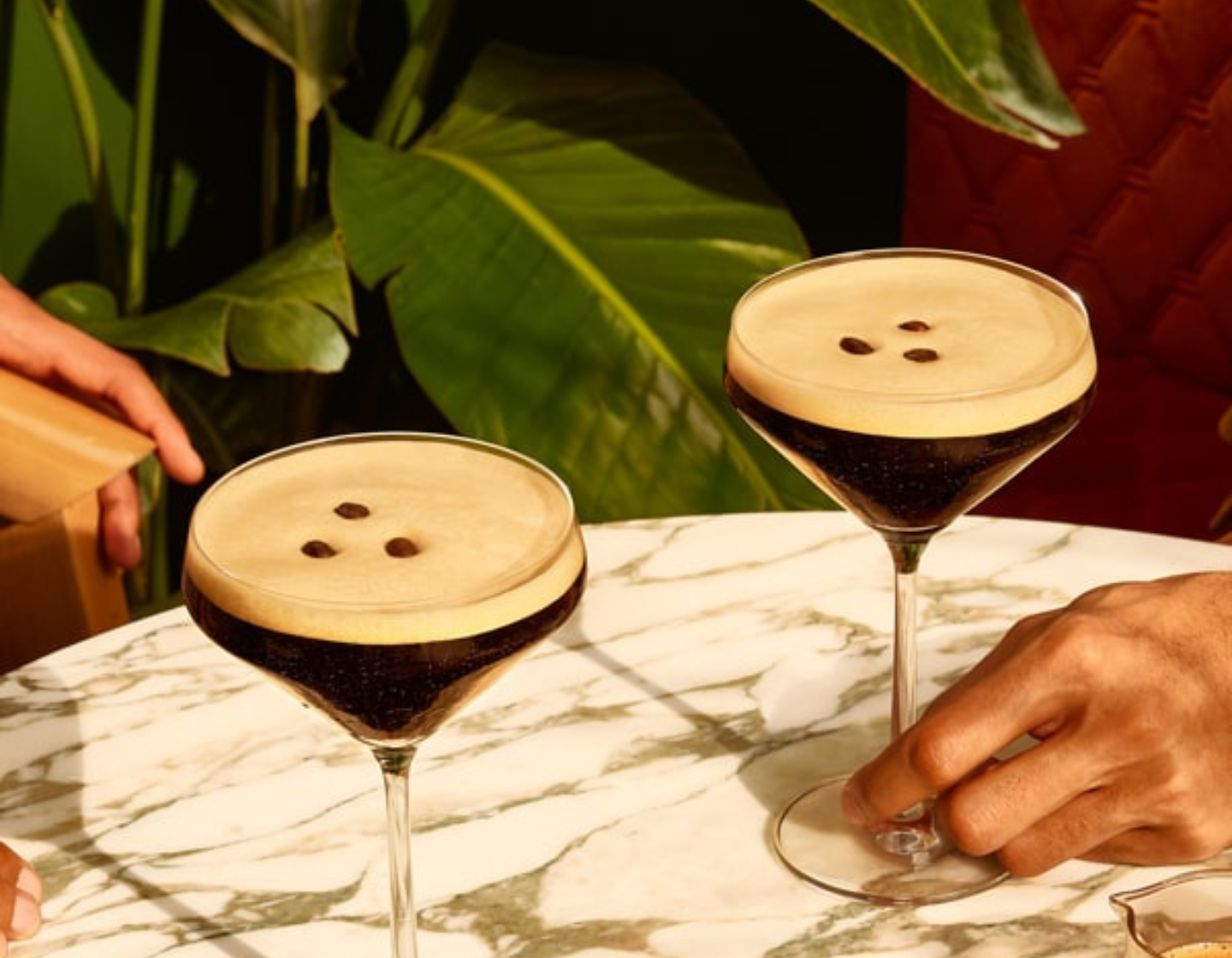 2 espresso martinis on a tsble with hands reaching