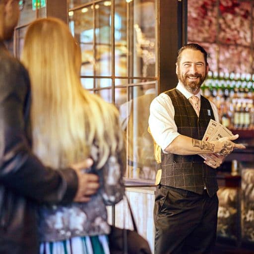 Un bartender saludando a un hombre y una mujer en un restaurante con una sonrisa amigable