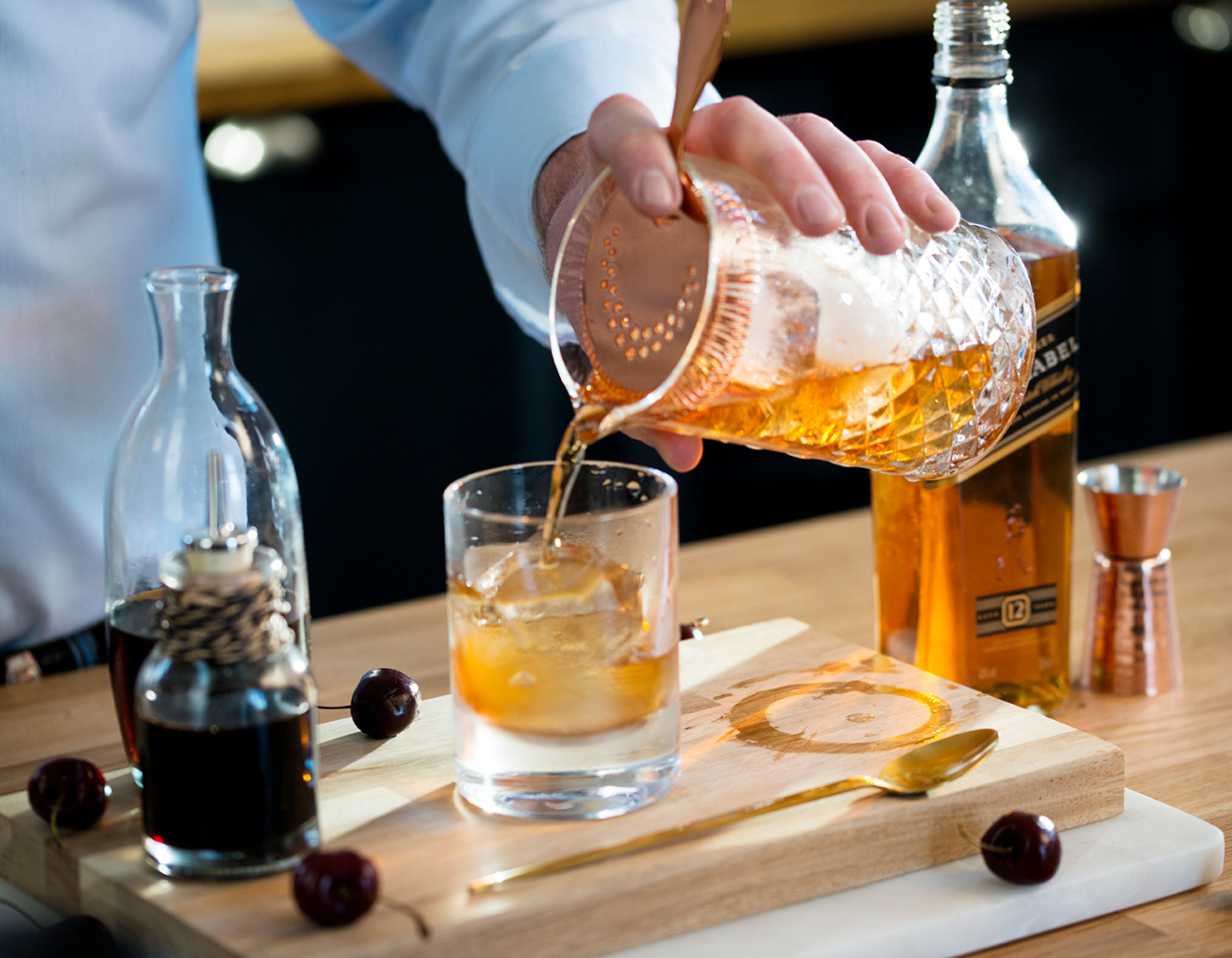 Whiskey cocktail being poured from shaker into glass with ice 