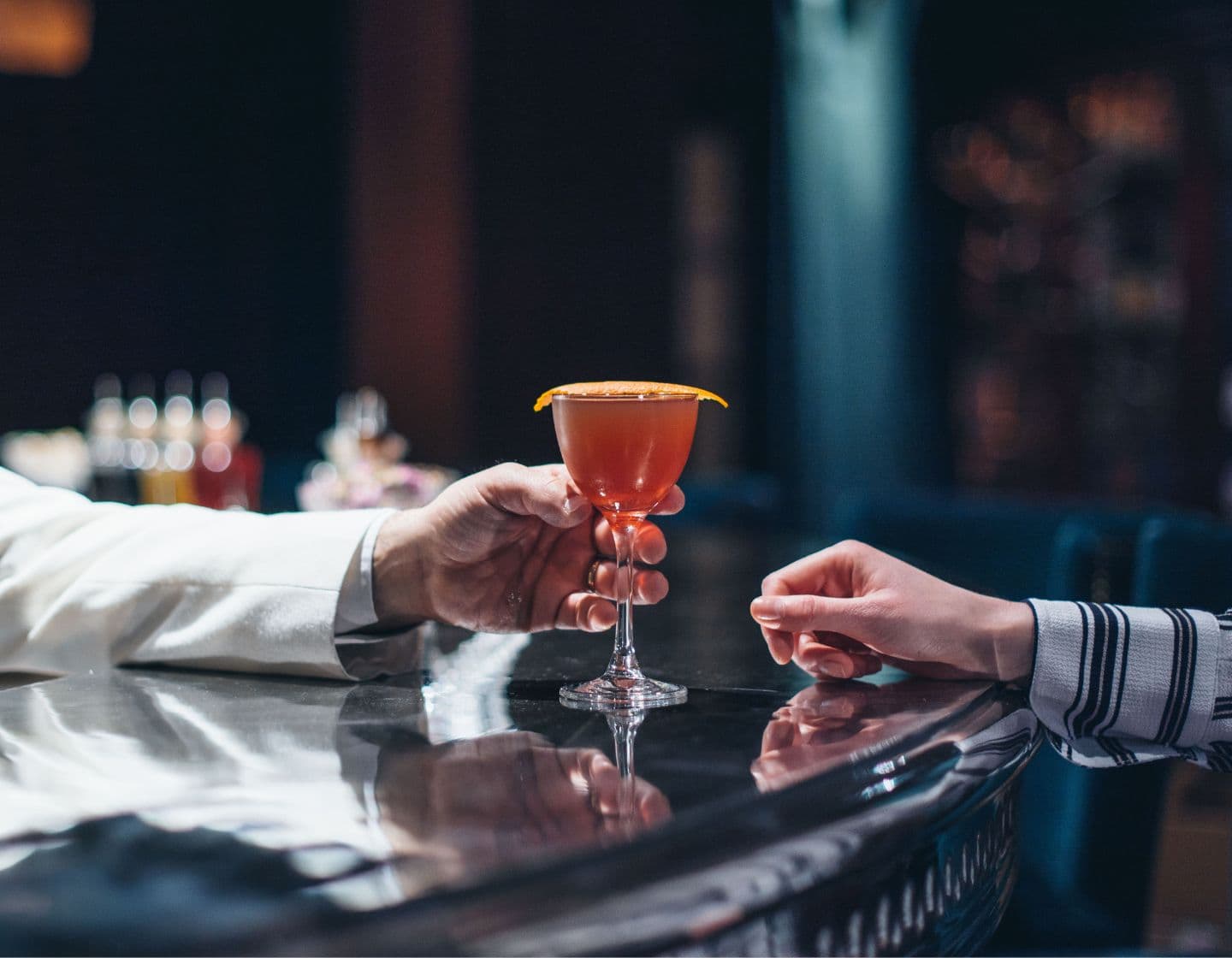 Man handing orange drink across bar