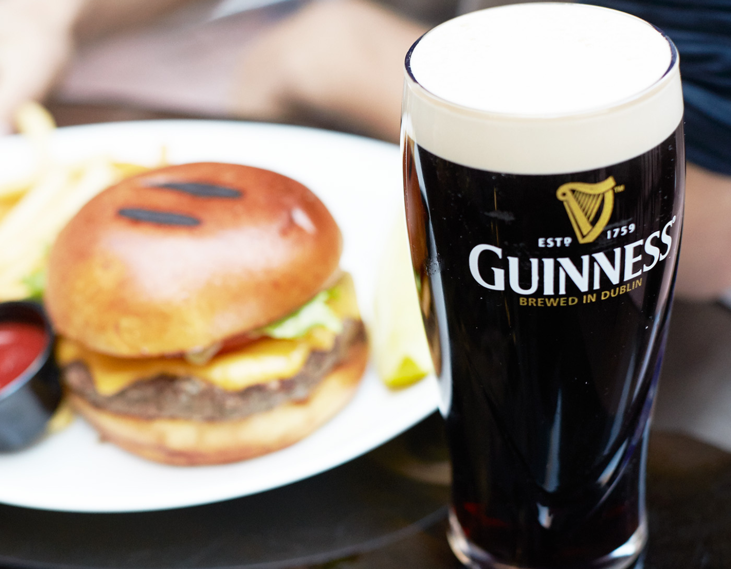 Pint of Guinness on table with burger and chips behind