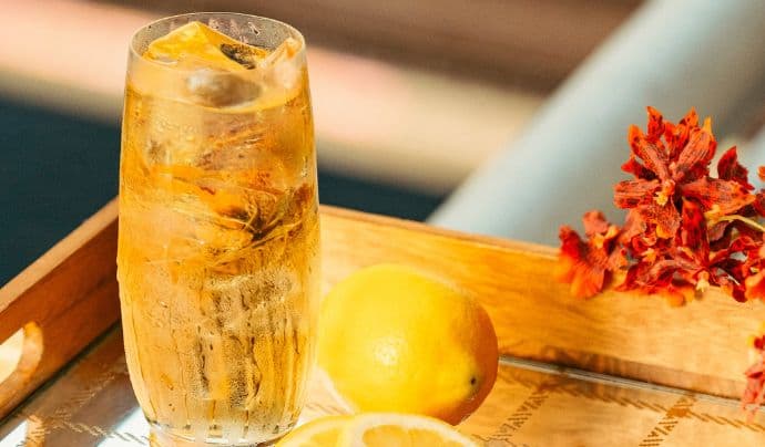 Uma bebida gelada em uma bandeja de madeira acompanhada por um limão 