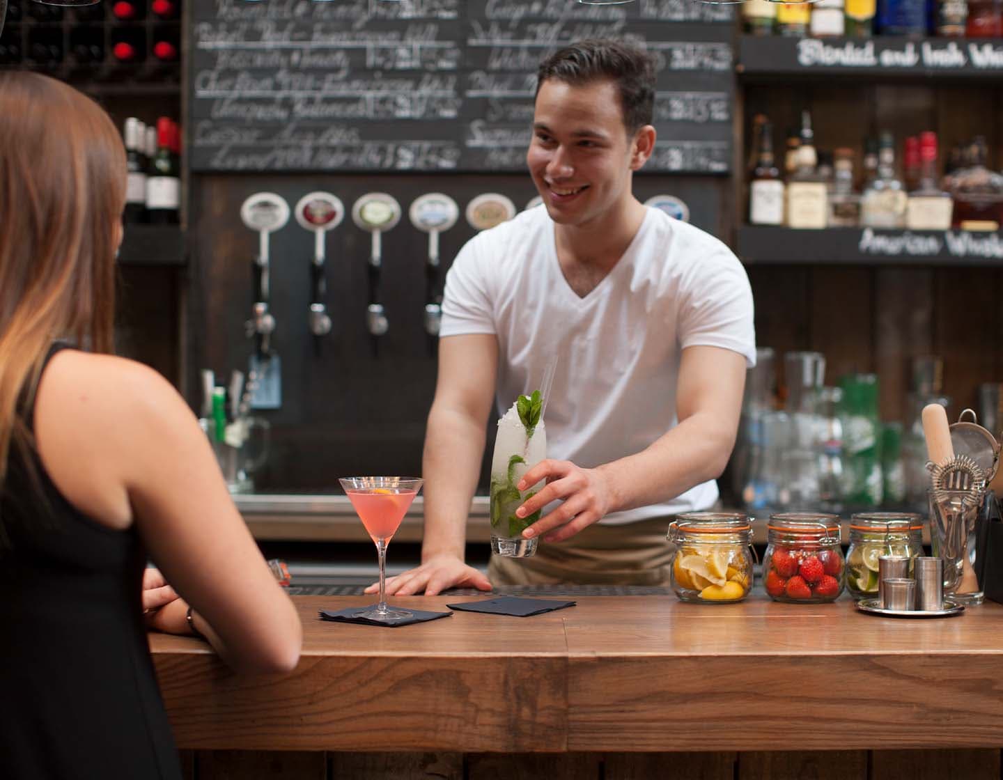 Ein Barkeeper serviert einer Kundin einen Cocktails an der Bar.