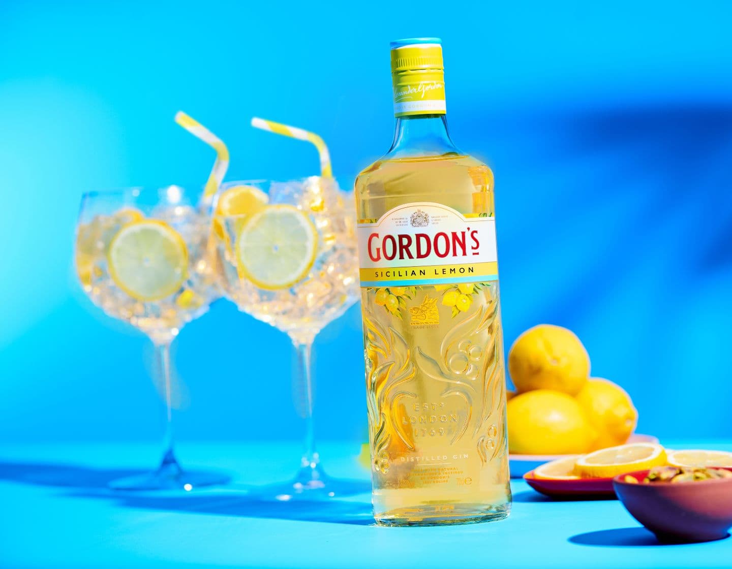  Bottle of Gordon’s Sicilian Lemon gin beside two G&T glasses against blue background 