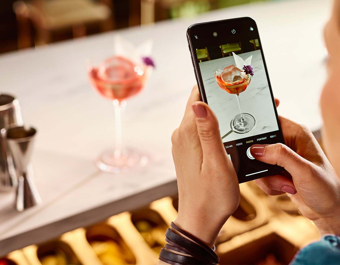 Primer plano de un bartender haciendo una foto de un cóctel con un smartphone.