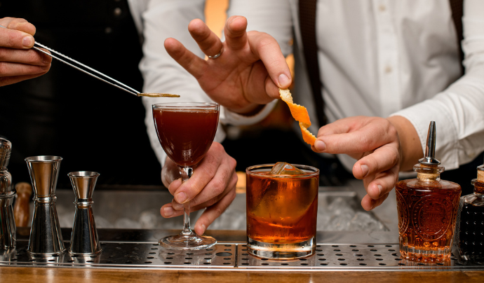 Two bartenders adding finishing touches to their serves using tongs to apply a lemon garnish.