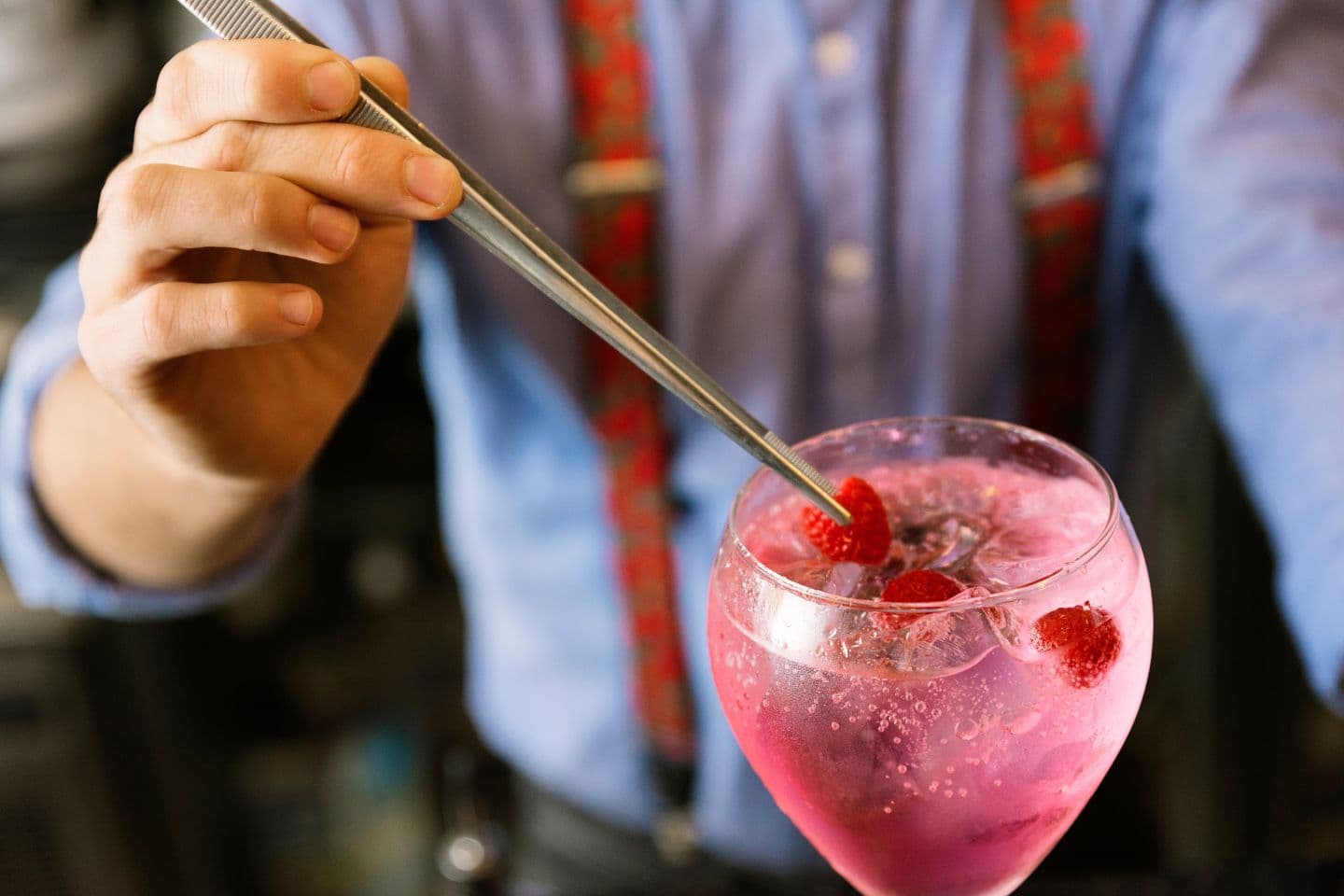 Garnsih being placed on the top of a pink cocktail.