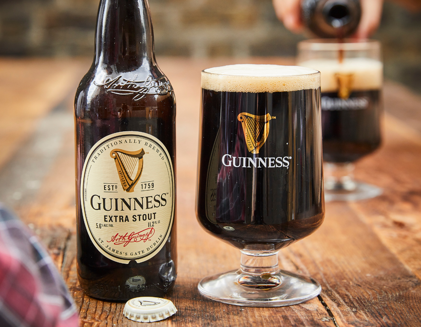 Botella de Guinness Extra Stout sobre la mesa junto a vaso de pinta lleno de Guinness