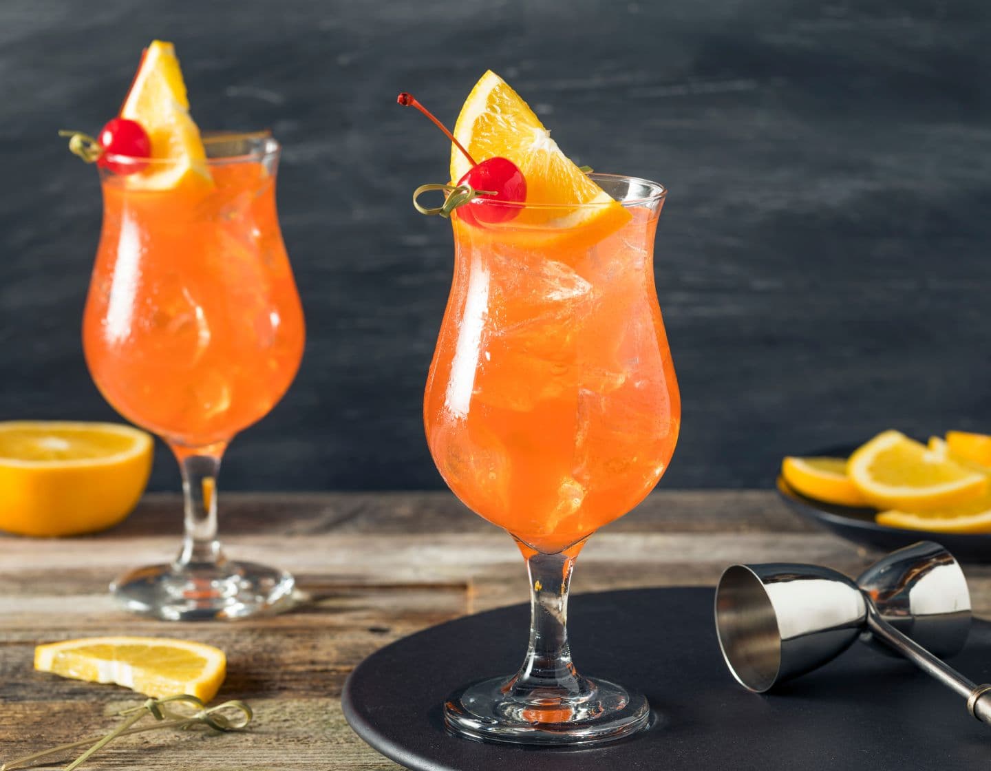 Two Singapore Slings surrounded by orange slices and garnished with an orange wedge and cherry 