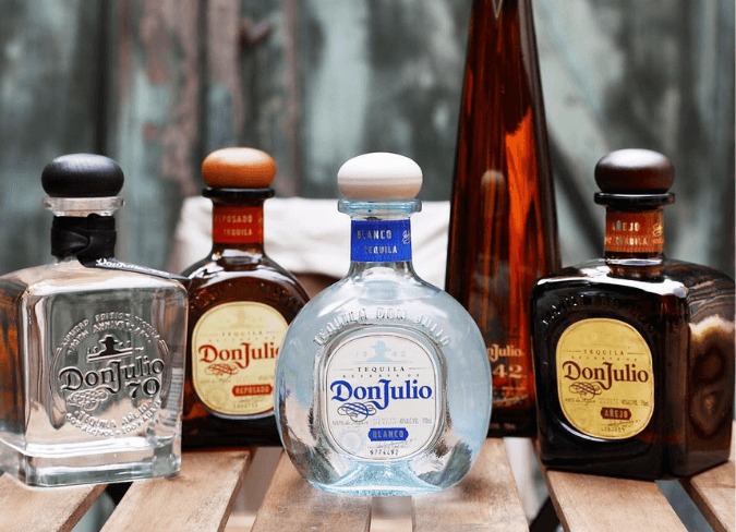 Seleção de diferentes garrafas de tequila Don Julio posicionadas sobre mesa de madeira