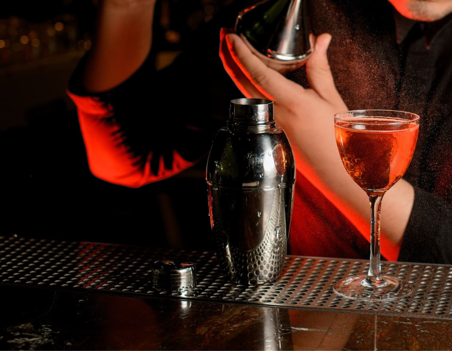 Ein rotes Getränk in einer dunklen Bar wird von einem Zerstäuber versprüht.