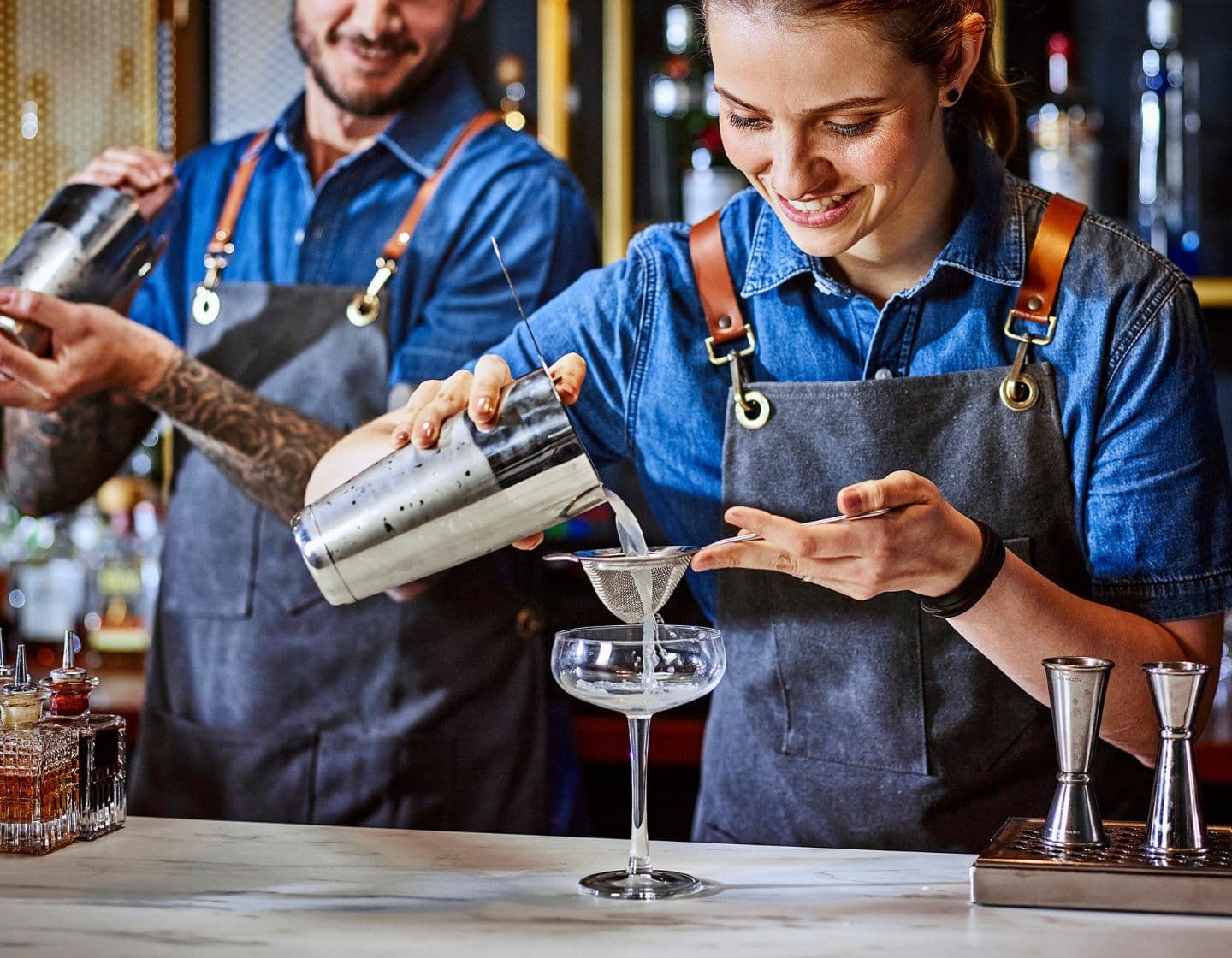 Bartenderes trabajando juntos, sirviendo un líquido de una coctelera a un vaso 